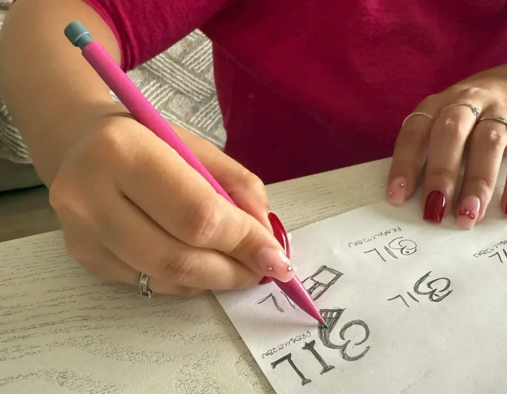 Main dessinant des croquis du futur logo d’O3il Production pour la nouvelle identité visuelle avec un crayon rose.