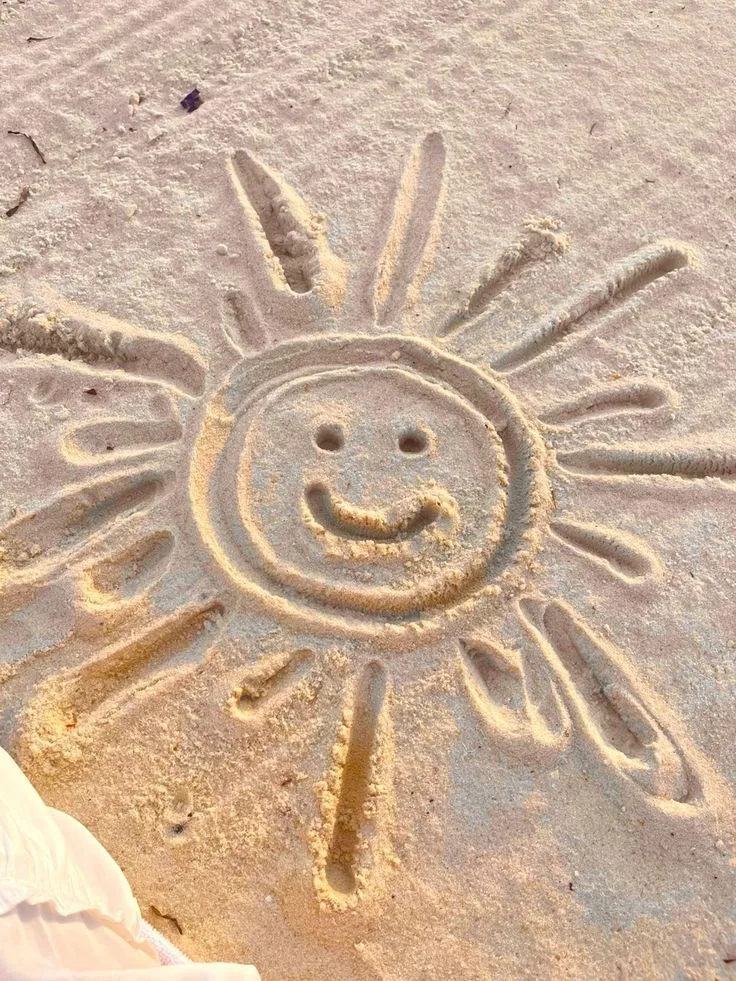 Un soleil souriant tracé dans le sable d’une plage