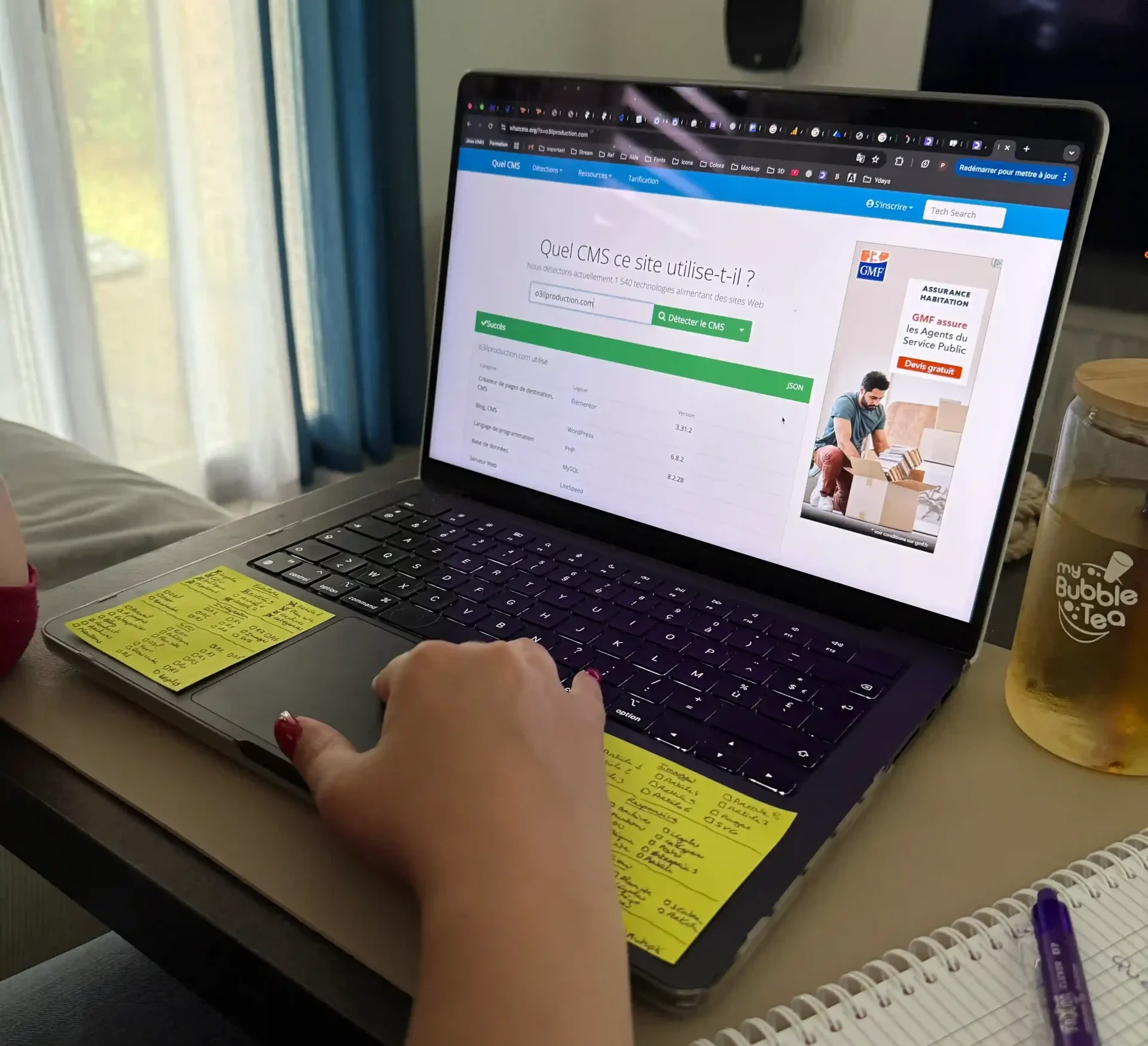 Main de Tiffanie utilisant un outil en ligne pour détecter le CMS d’un site web avant de travailler sur son référencement.