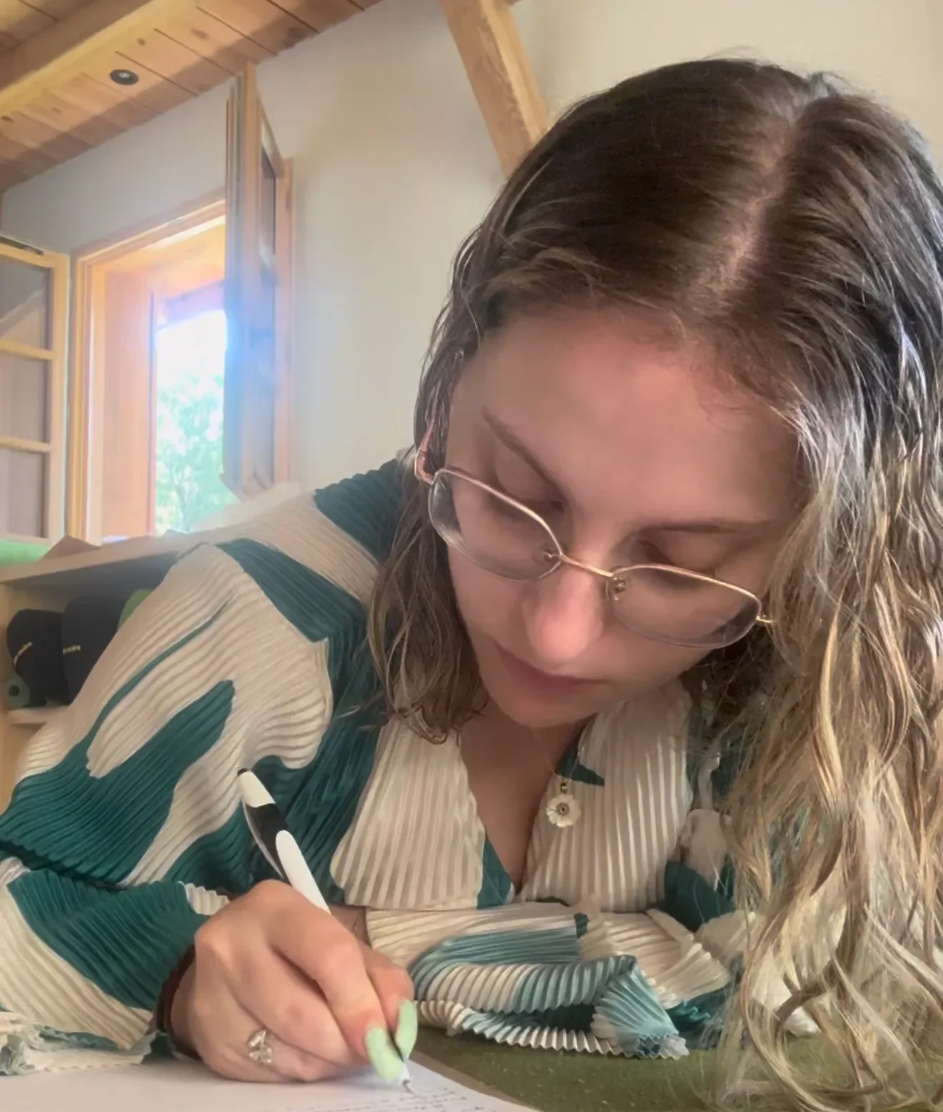 Photo pour le blog de Tiffanie qui est concentrée, écrivant à la main avec un stylo, lumière naturelle en arrière-plan
